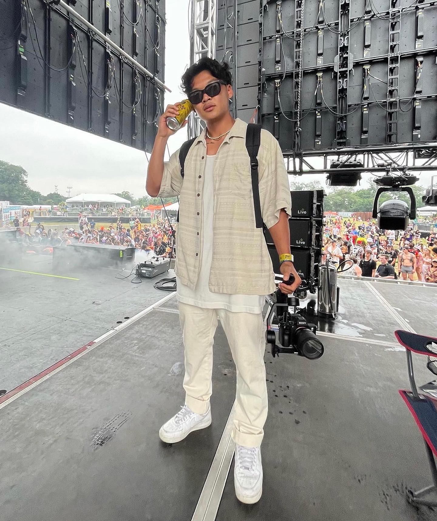 Soso on stage at Heat Wave holding a camera and a Yerba Mate can, with the festival crowd behind him